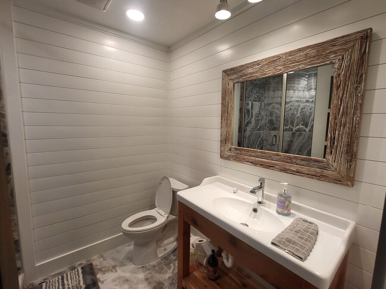 Un bany amb un vàter blanc, un lavabo amb un mirall a sobre i un moble de bany de fusta.