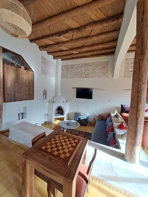 A cozy living room with a wooden ceiling, a fireplace, a TV, and a chess table. - La Maison Mady (Ounagha)
