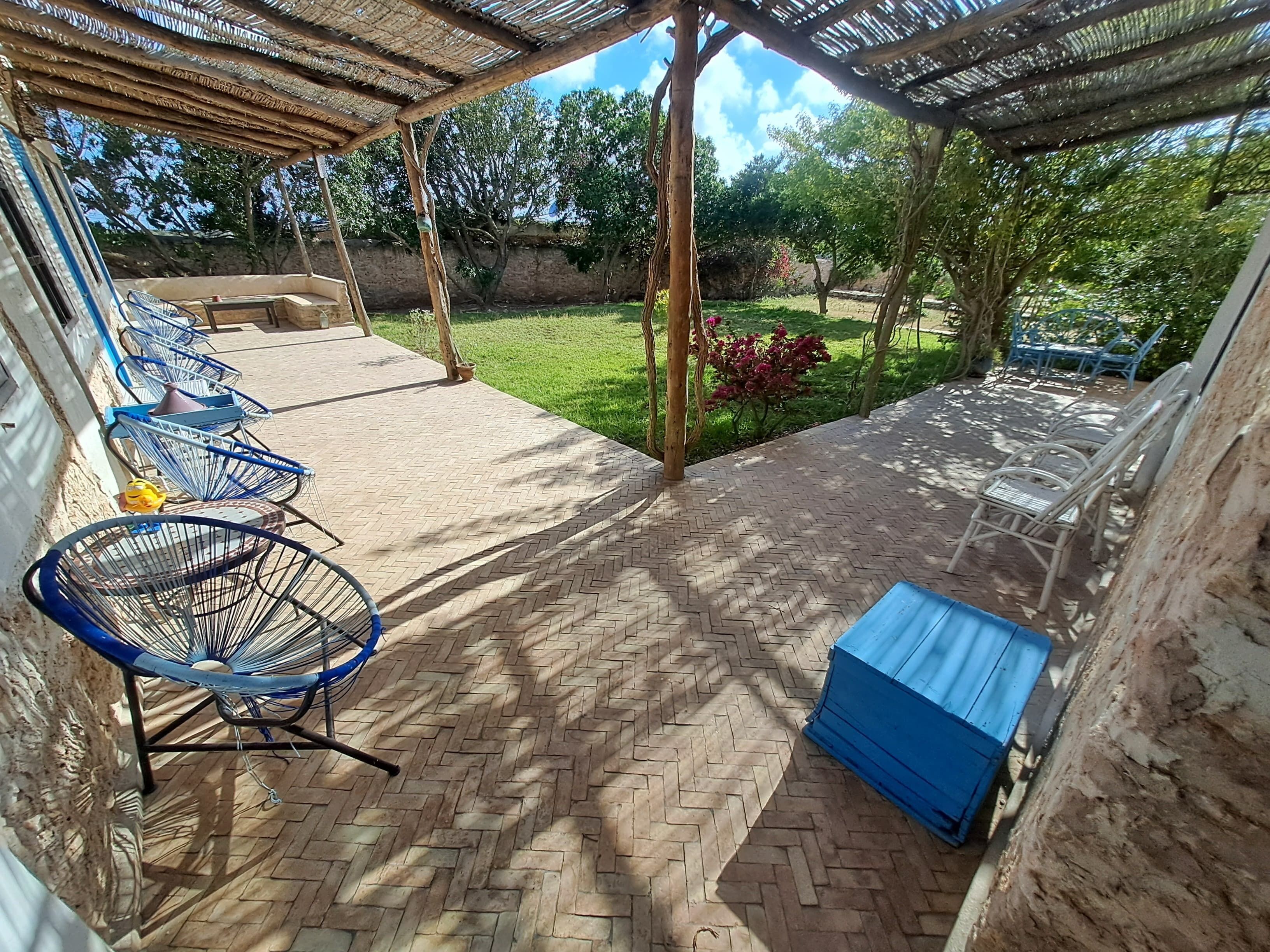 Ein überdachter Patio-Bereich mit Terrazzo-Boden, blauen Metallstühlen und einer blauen Aufbewahrungsbox.