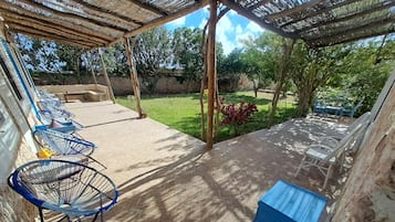 Ein überdachter Patio-Bereich mit Terrazzo-Boden, blauen Metallstühlen und einer blauen Aufbewahrungsbox.