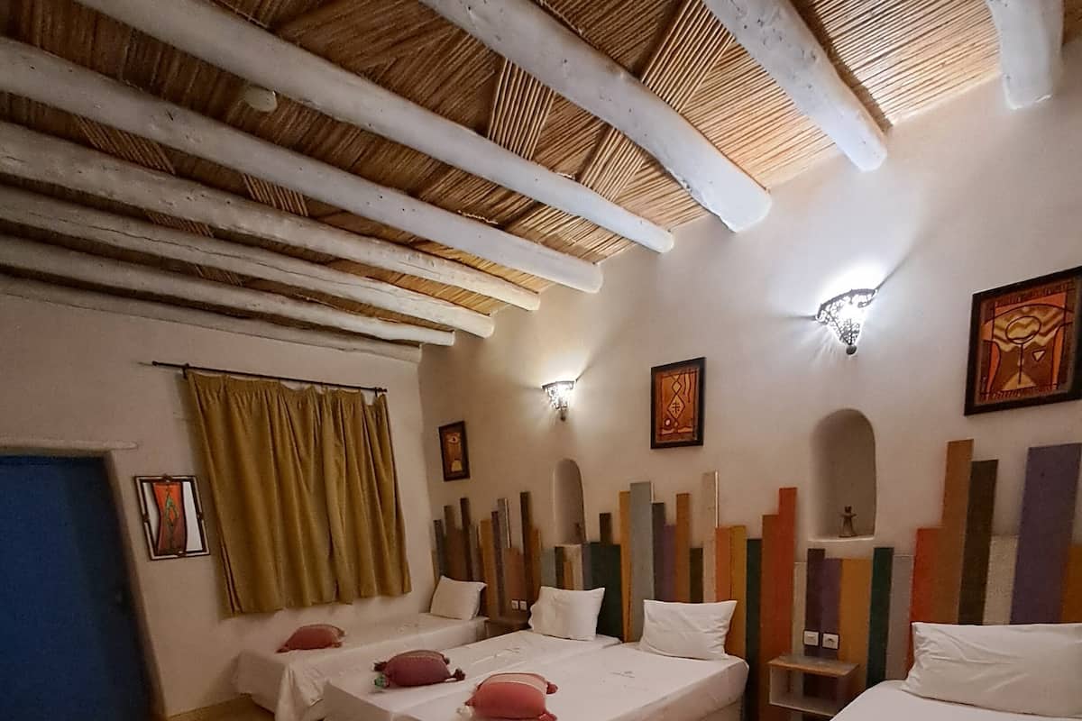 A room with two beds, a patterned rug, a wooden ceiling, and a wall with colorful vertical elements.