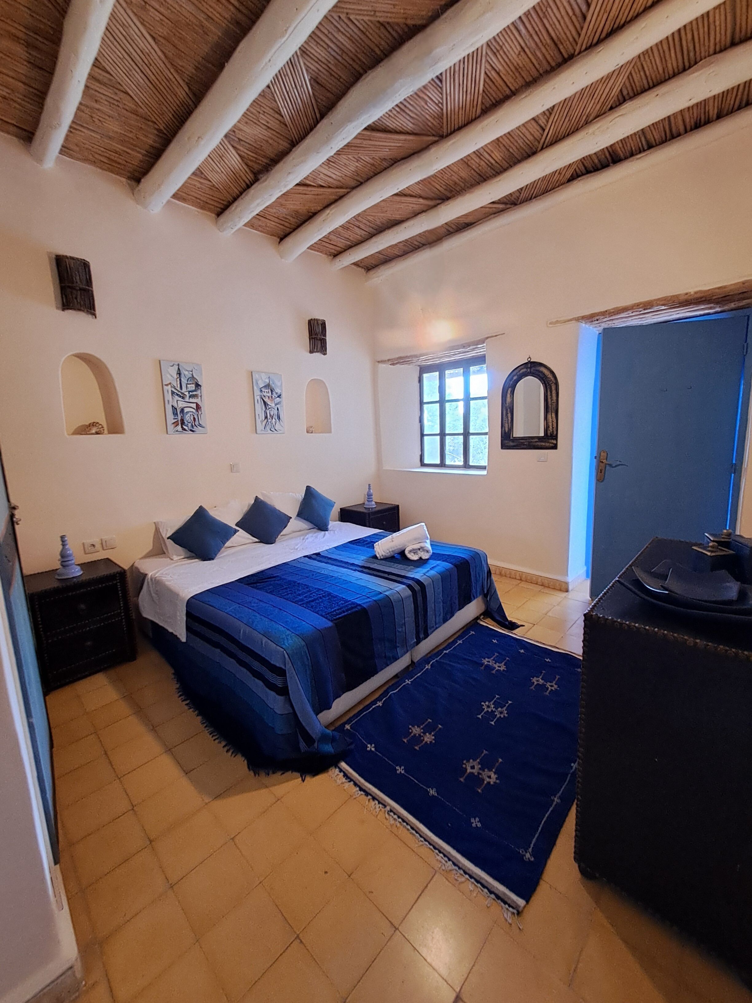 A bedroom with a bed, a nightstand, a dresser, a window, and a door.