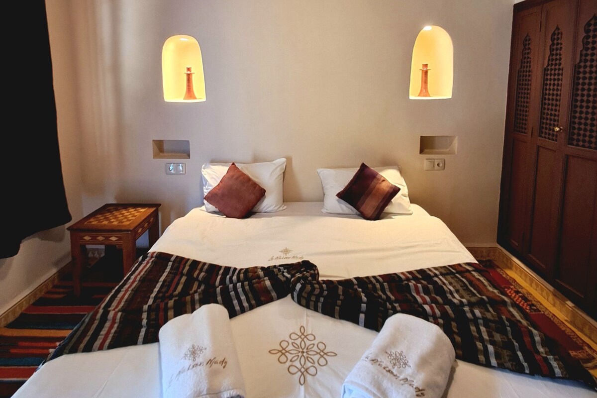 A hotel room with a bed, two bedside lamps, a nightstand, and a patterned carpet.
