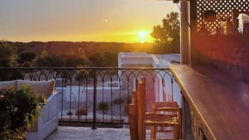 Ein Balkon mit Blick auf den Sonnenuntergang, ein Holzsessel und eine weiße gepolsterte Bank.