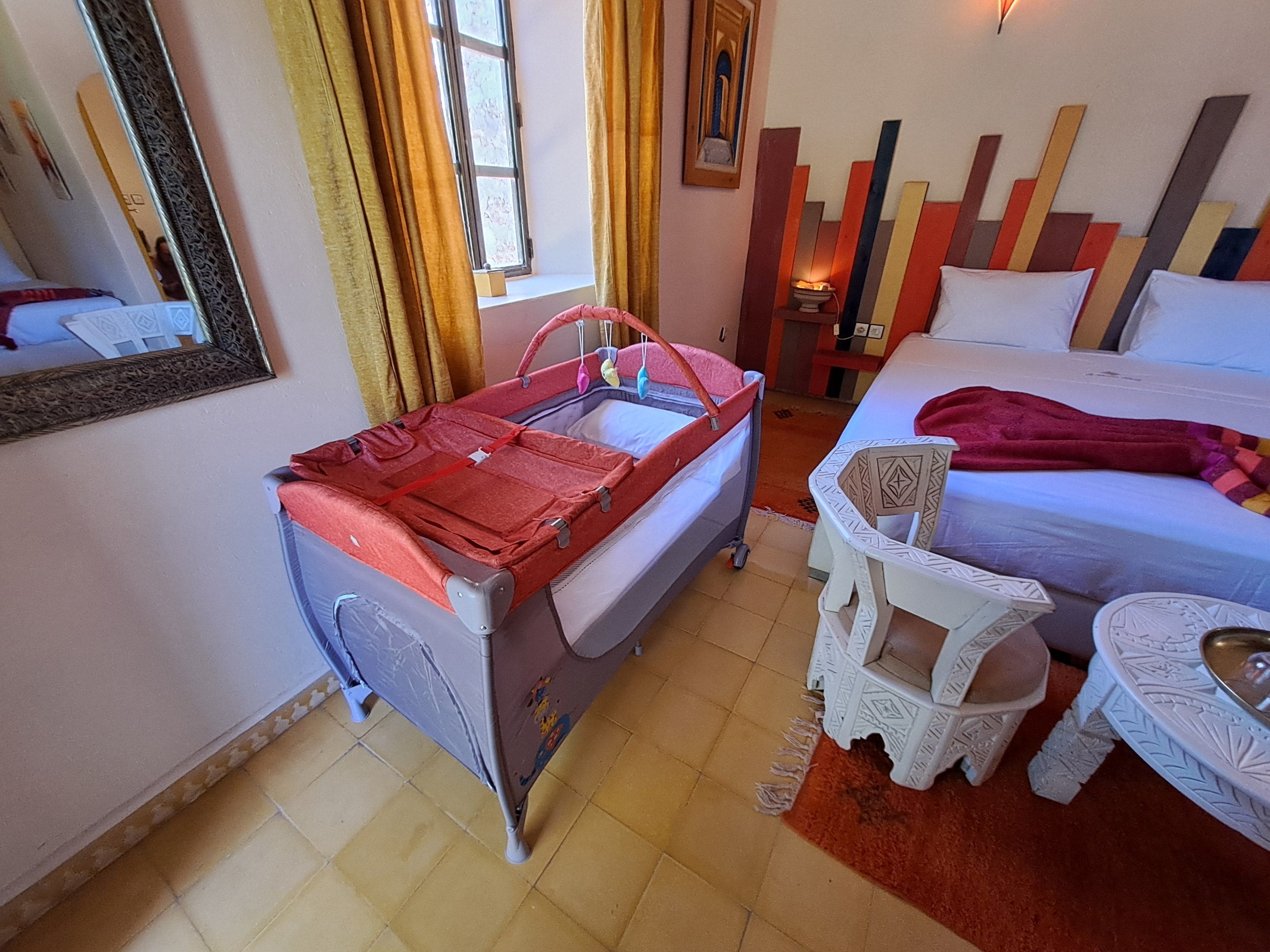 Une chambre à coucher avec un lit, une petite table, une chaise, un miroir et une fenêtre avec des rideaux.