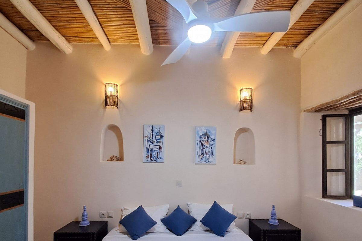 A bedroom with a bed, two nightstands, a ceiling fan, and wall-mounted lights.