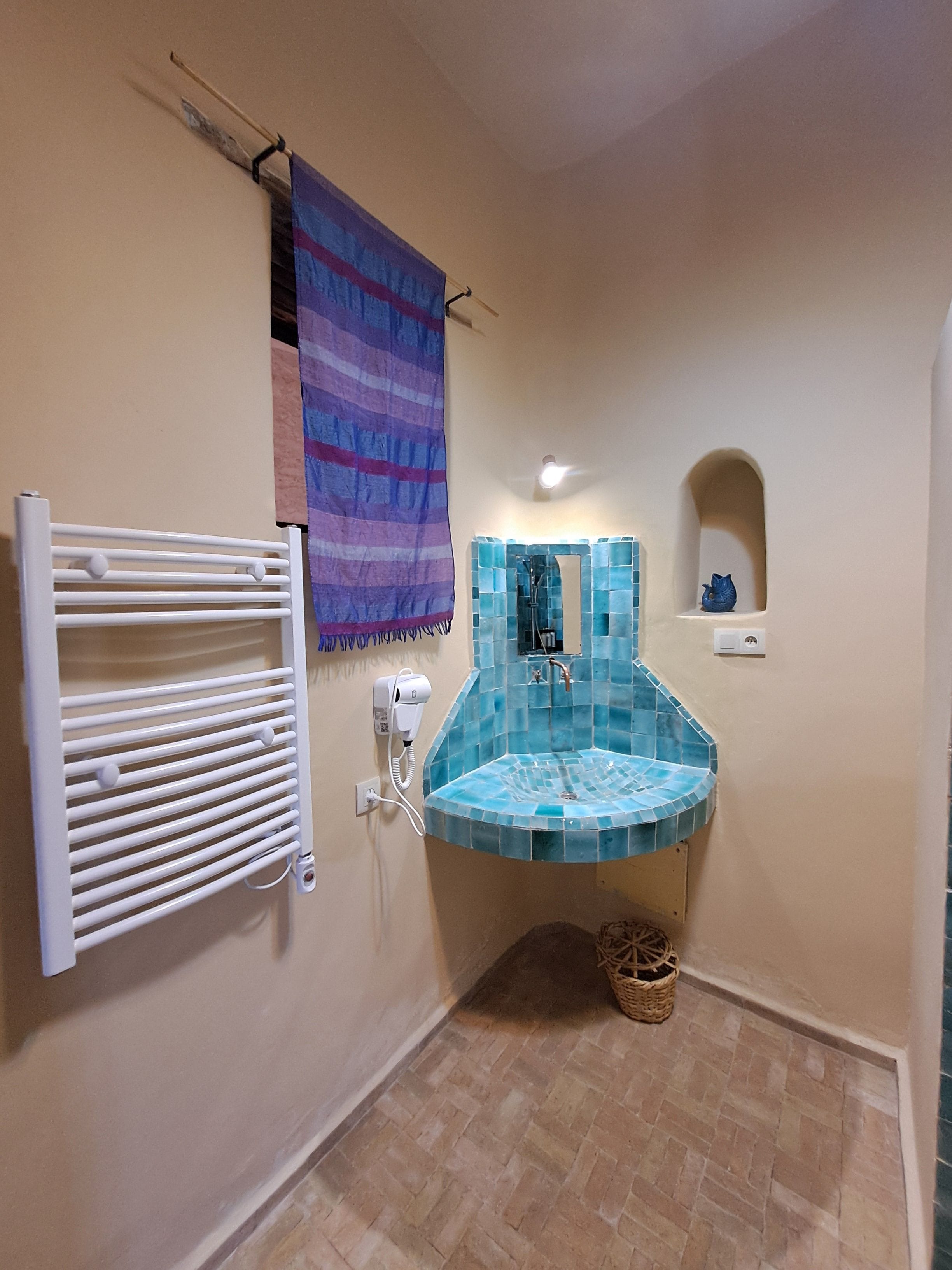 Un baño con lavamanos azulejado, un perchero y un calentador de pared.