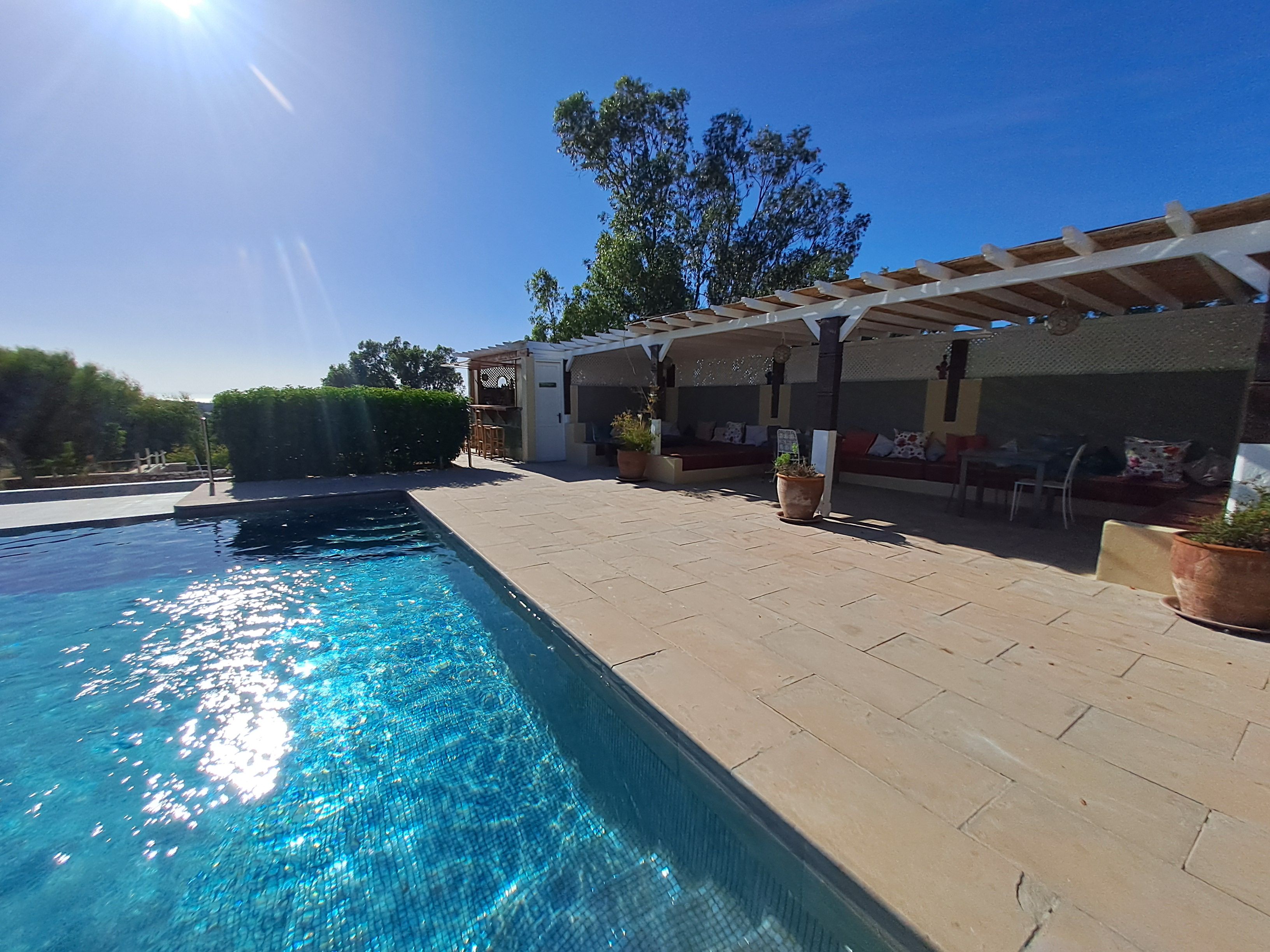 Piscina com pergolado e área de estar ao ar livre.