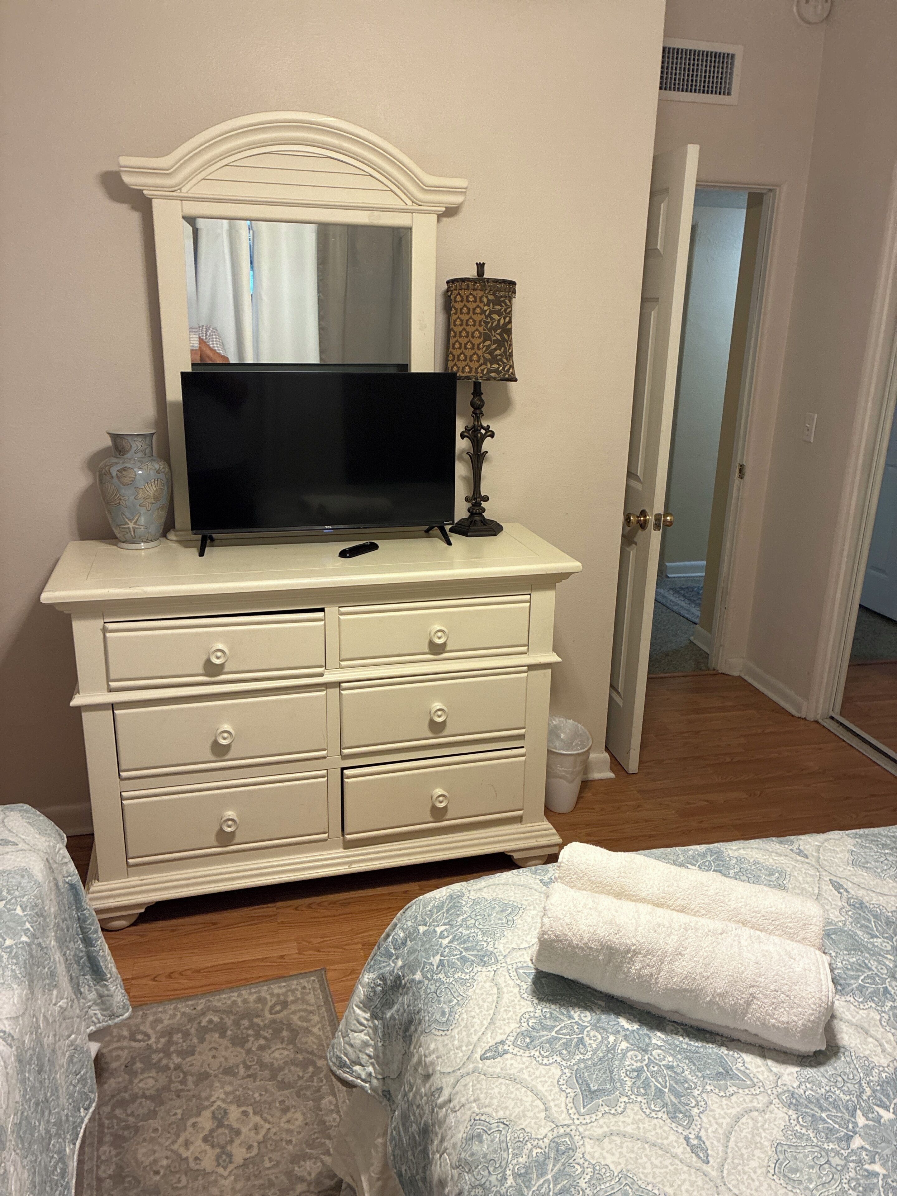 A bedroom with a dresser, a television, a lamp, and a bed with a patterned bedspread.