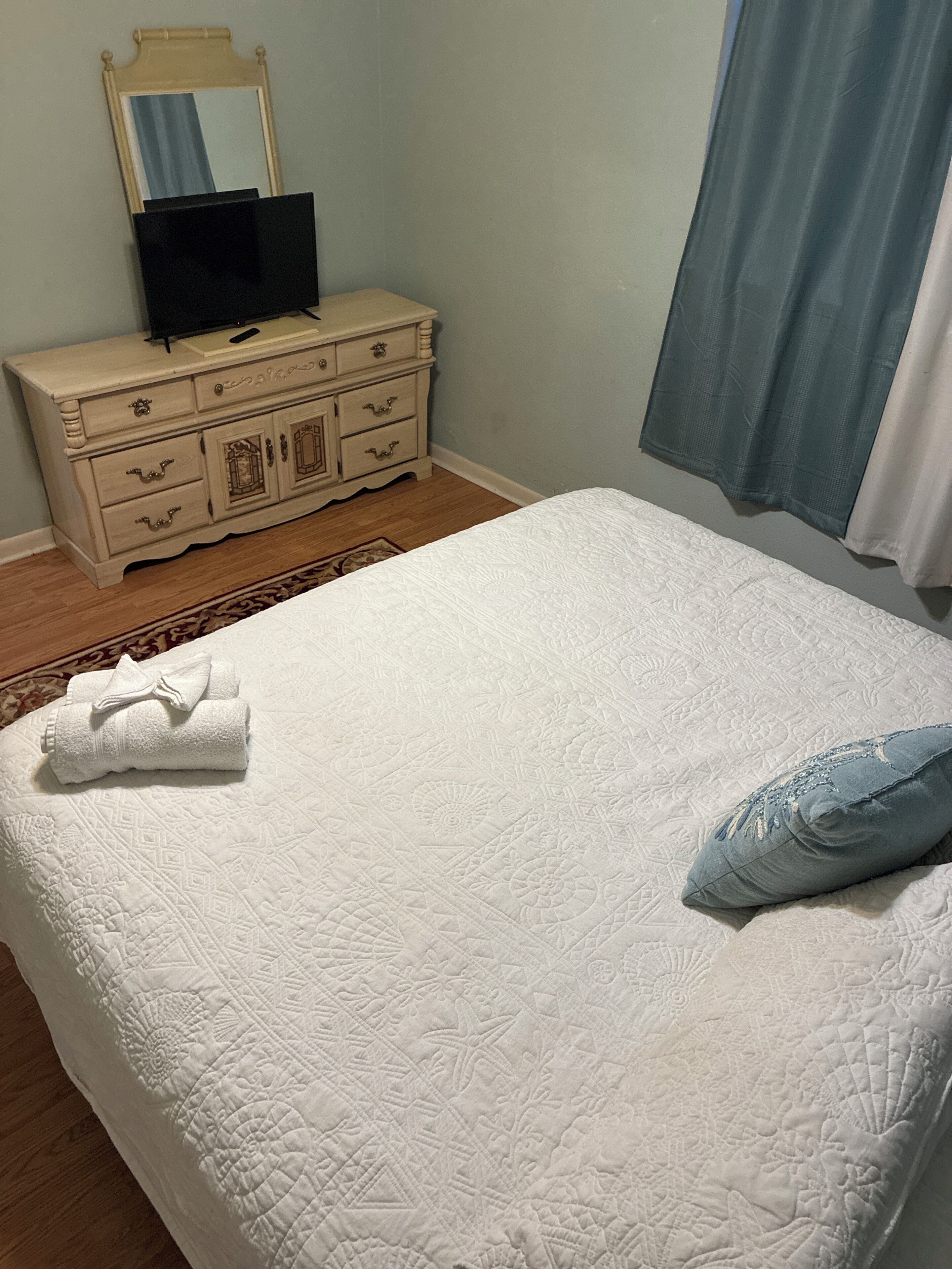 Un dormitorio con cama, cómoda, espejo y ventana con cortinas.