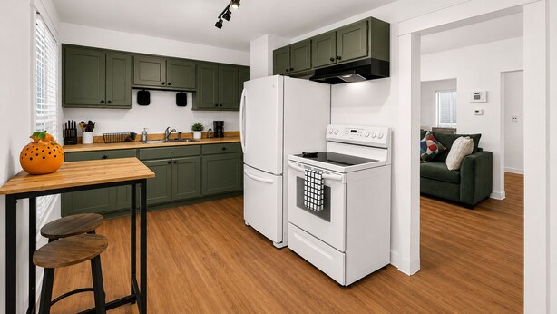 A compact kitchen with green cabinets, a white refrigerator, a stove, and a wooden dining table with stools. - Willow & Mist - Gorgeous 3-bedroom house minutes from Niagara Falls attractions (Niagara Falls)