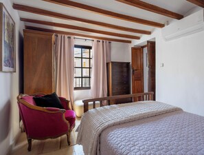 Une chambre à coucher avec un lit, une armoire en bois, une chaise et une fenêtre avec des rideaux.