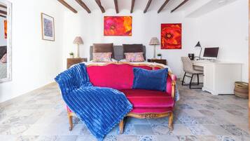 A room with a red velvet sofa, a blue throw, a wooden desk, and a computer.