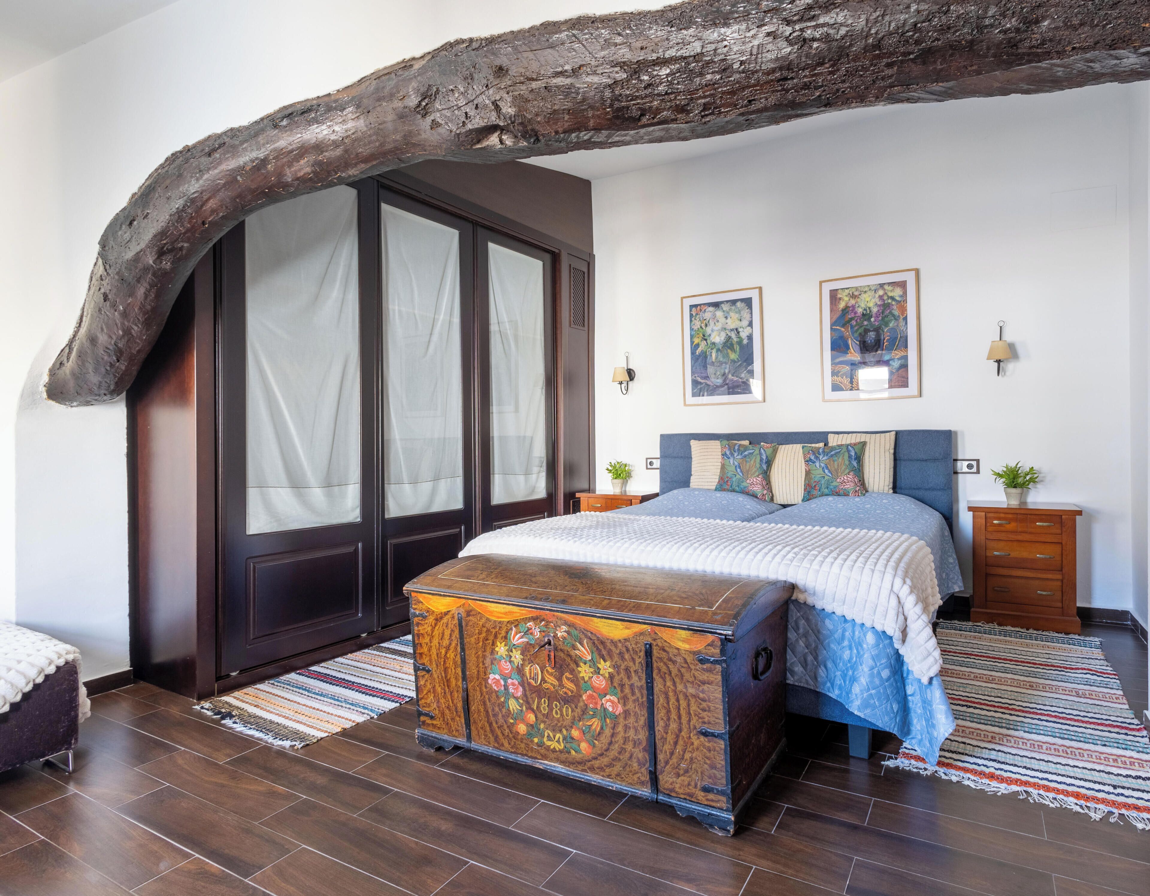 Een slaapkamer met een groot bed, een houten kist, een garderobe en een plafond van een bijzondere tak.