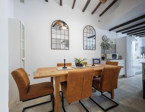 A dining area with a wooden table, brown upholstered chairs, two arched mirrors, and a potted plant.