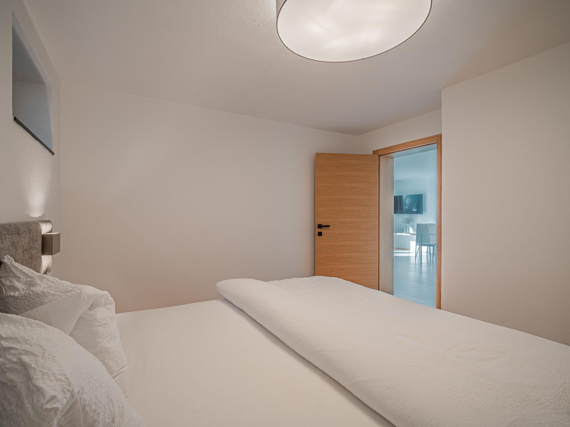 Un dormitorio minimalista con una cama, una puerta de madera y vistas a un comedor.