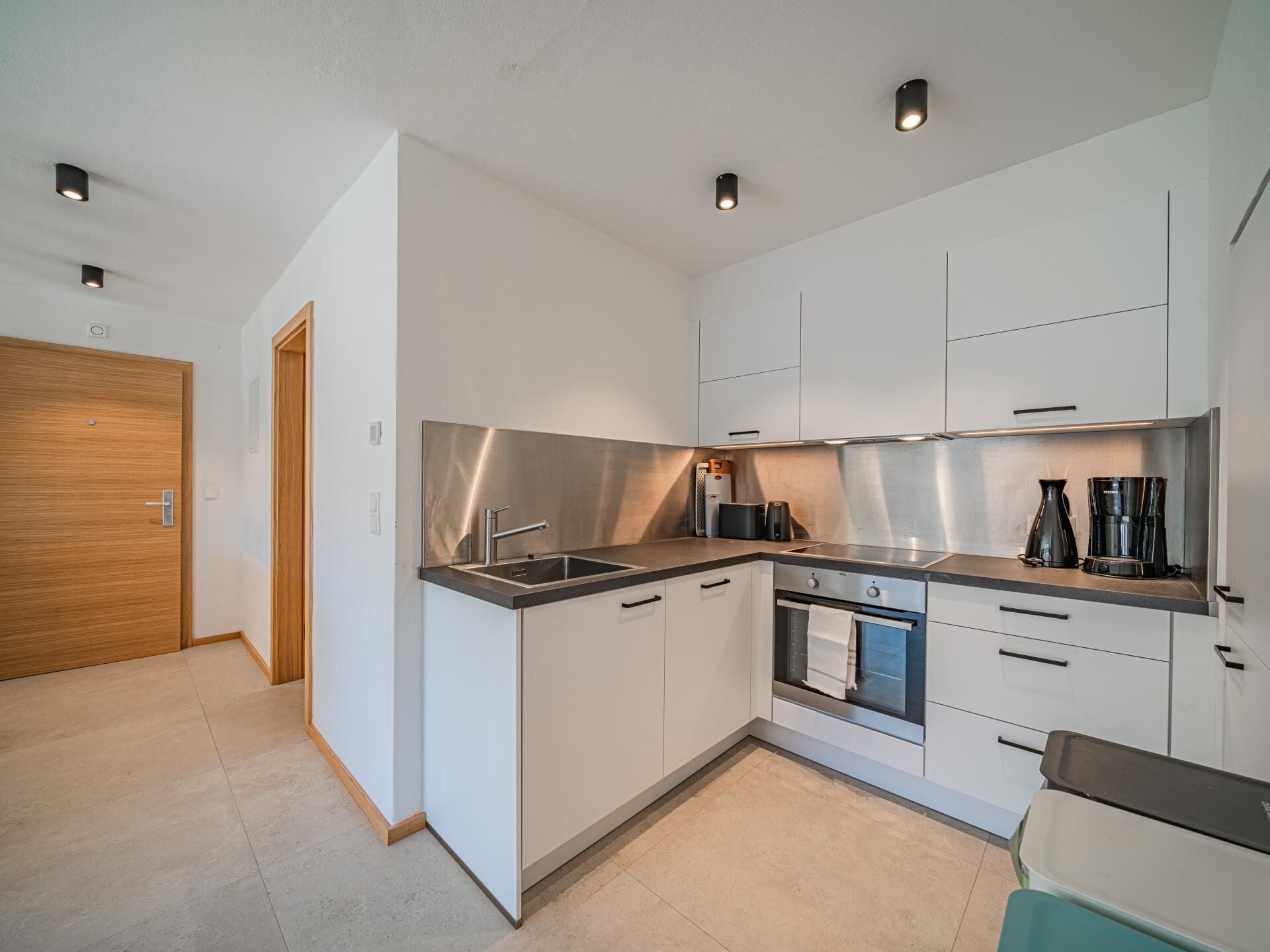Una cocina moderna con armarios blancos, electrodomésticos de acero inoxidable y una puerta de madera.