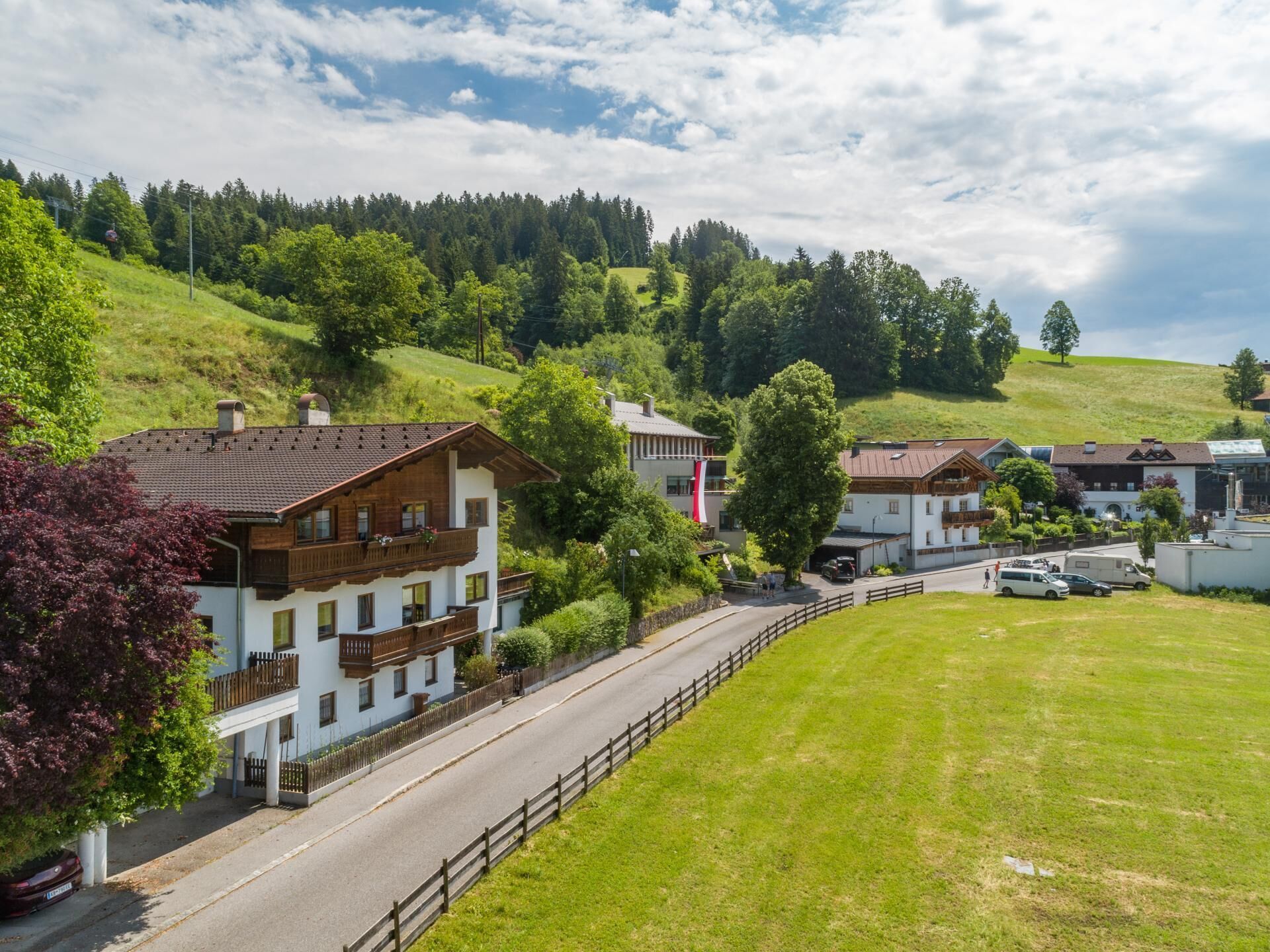 En landlig landsby med traditionelle huse, en belagt vej og en grøn bakke i baggrunden.