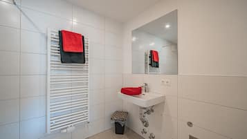 Een moderne badkamer met witte tegels, een witte radiator, een wastafel met een rode handdoek en een spiegel.