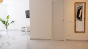 A modern interior with a white door, a potted plant, a small table, and a mirror reflecting a wardrobe. - Modern 3 bed apt, walking distance to Puerto Banus (Marbella)