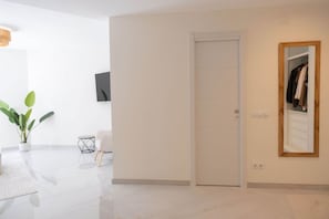 Ein modernes Interieur mit einer weißen Tür, einem Blumentopf, einem kleinen Tisch und einem Spiegel, der eine Garderobe widerspiegelt.