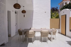 Eine Terrasse mit einem weißen Tisch, Korbstühlen, einer weißen Wand und einem Holzzaun.