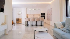 A modern living room with a sofa, a round coffee table, and a kitchen area with bar stools. - Modern 3 bed apt, walking distance to Puerto Banus (Marbella)