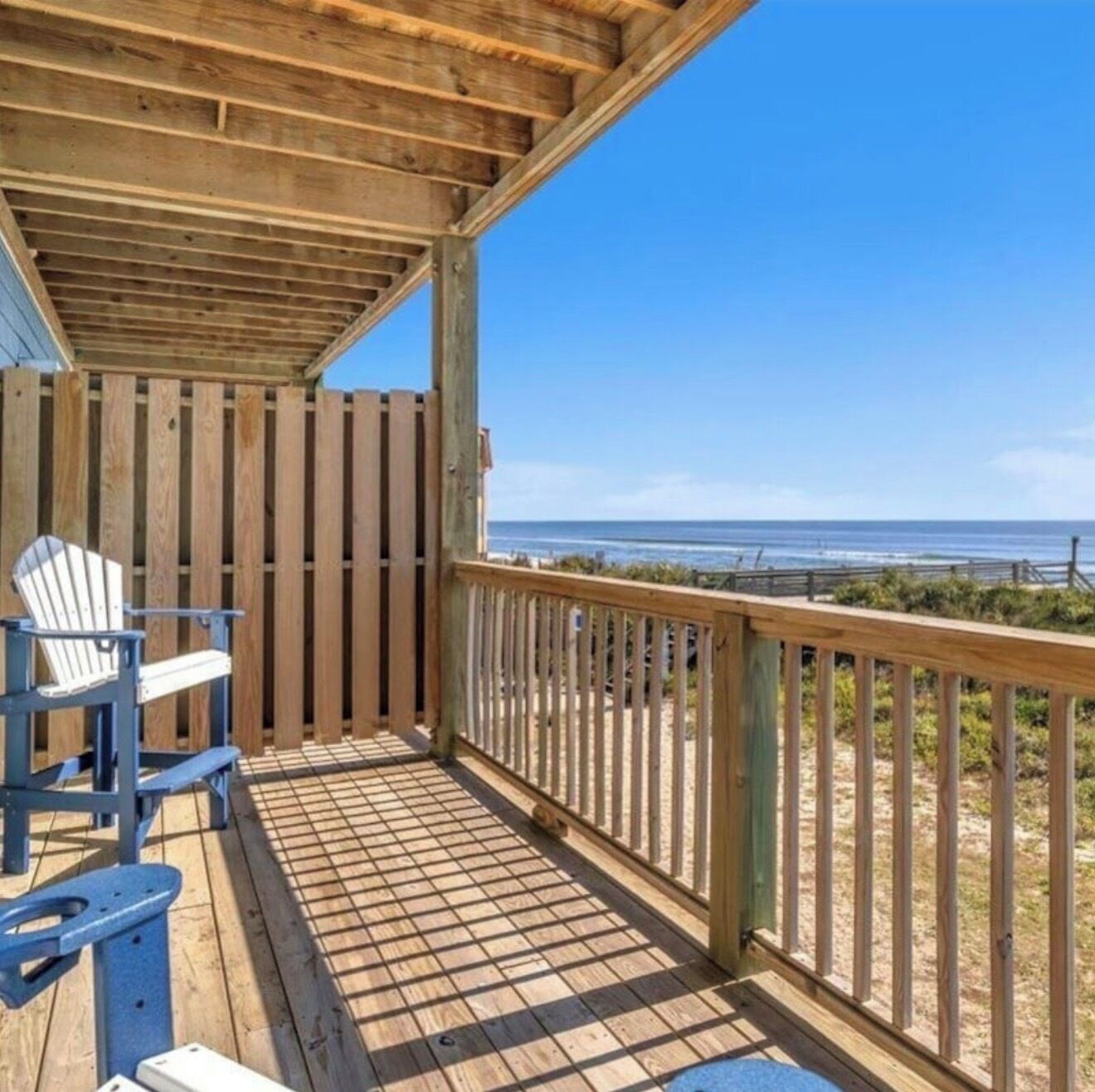 Eine Holzterrasse mit Geländer, ein blauer Adirondack-Sessel und Blick aufs Meer.