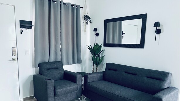 Un saló modern amb un sofà gris, un butaca a joc, un mirall gran i una planta en test.