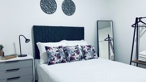 Un llit ben arropat amb almoinades florals, una taula de nit amb una làmpada, un mirall i una estant per a roba.