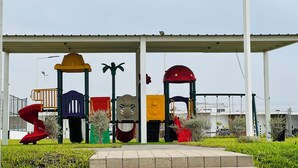 Un parc infantil amb diverses estructures de joc, una zona d'assecament i un camí pavimentat.