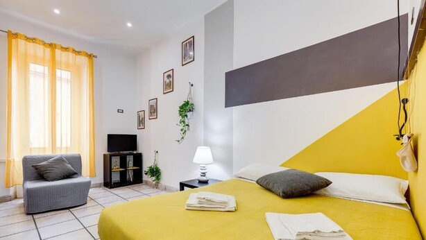 Ein Hotelzimmer mit Bett, einer Couch, einem Fernseher, einer Lampe und gerahmten Bildern an der Wand.
