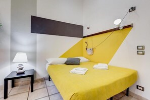 Ein Zimmer mit einem Bett, einem Nachttisch, einer Lampe und einer Wandleuchte.