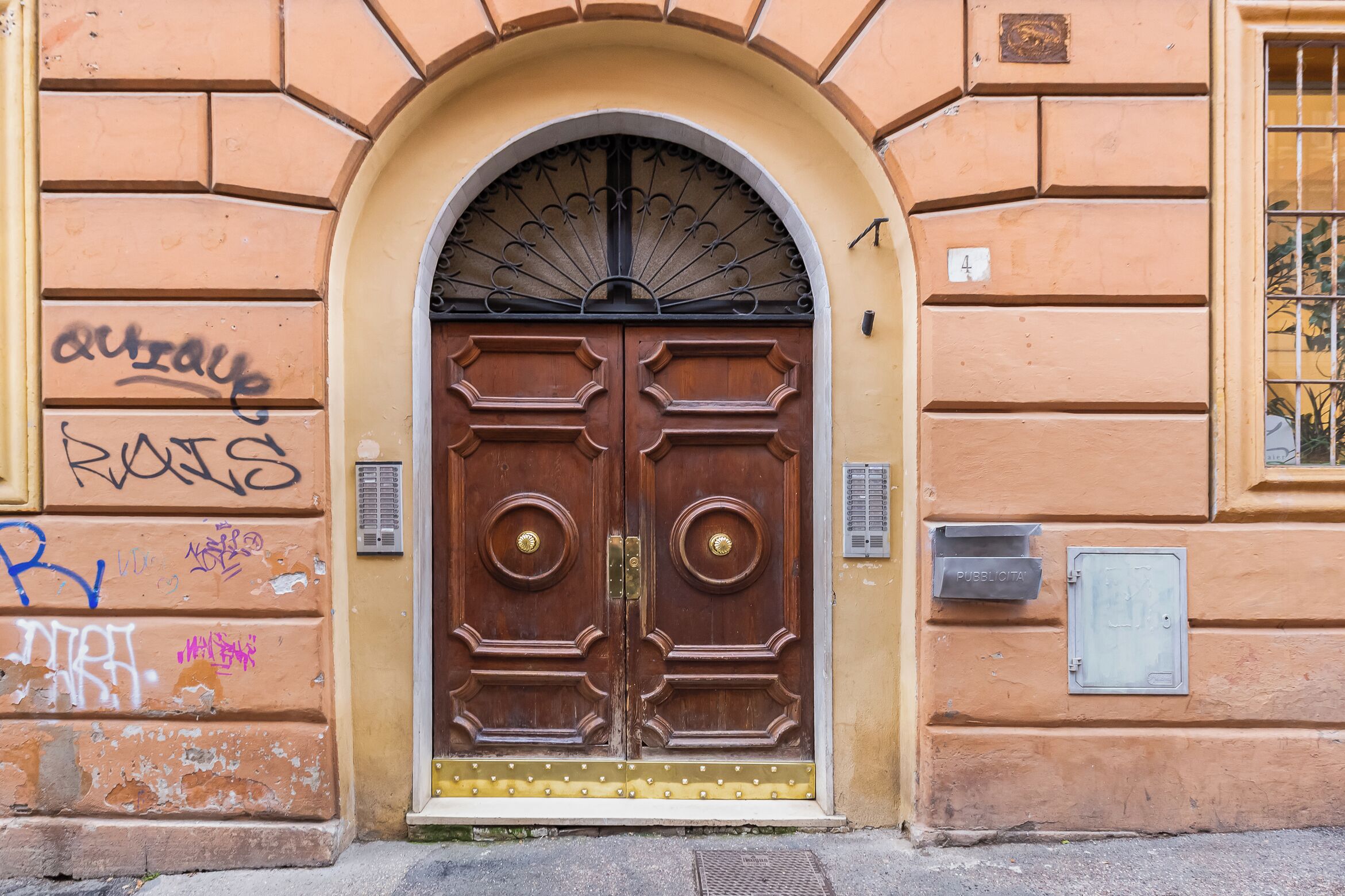 A double wooden door with a decorative arch above it, a mailbox, and a wall with graffiti.