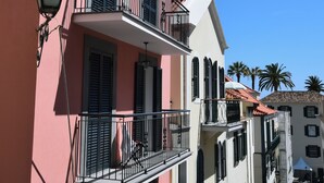 Un edifici rosa amb un balcó, un edifici blanc amb teulada vermella i un carrer amb palmeres.