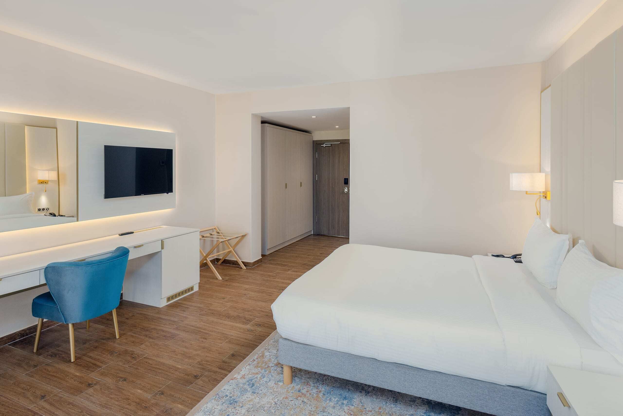 A hotel room with a bed, a desk, a chair, a TV, and a door.