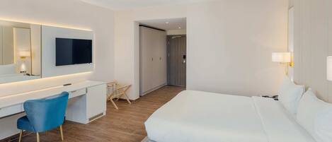A hotel room with a bed, a desk, a chair, a TV, and a door.