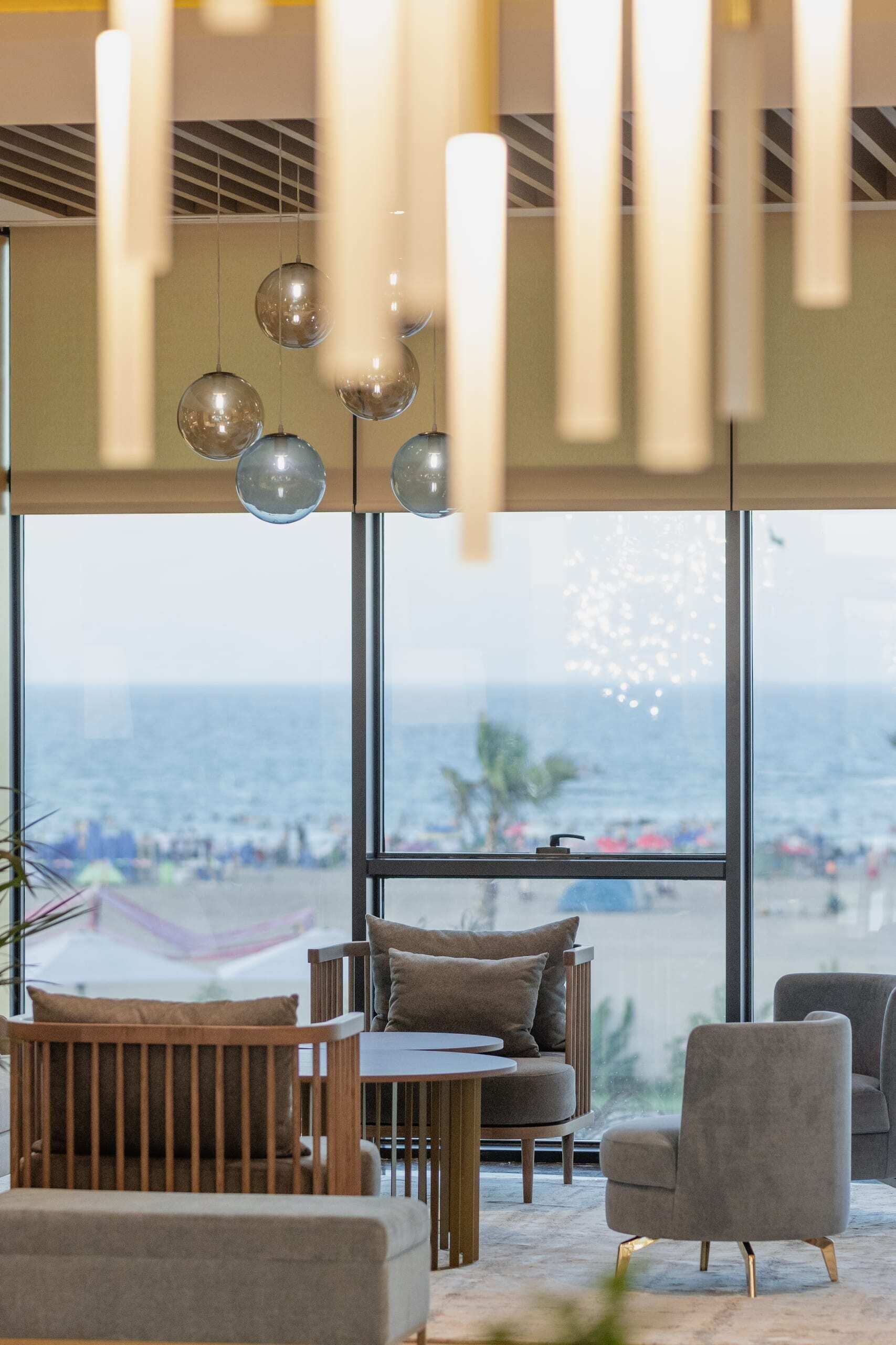 A modern interior with a view of the beach, featuring a seating area with a table and chairs, and pendant lighting.
