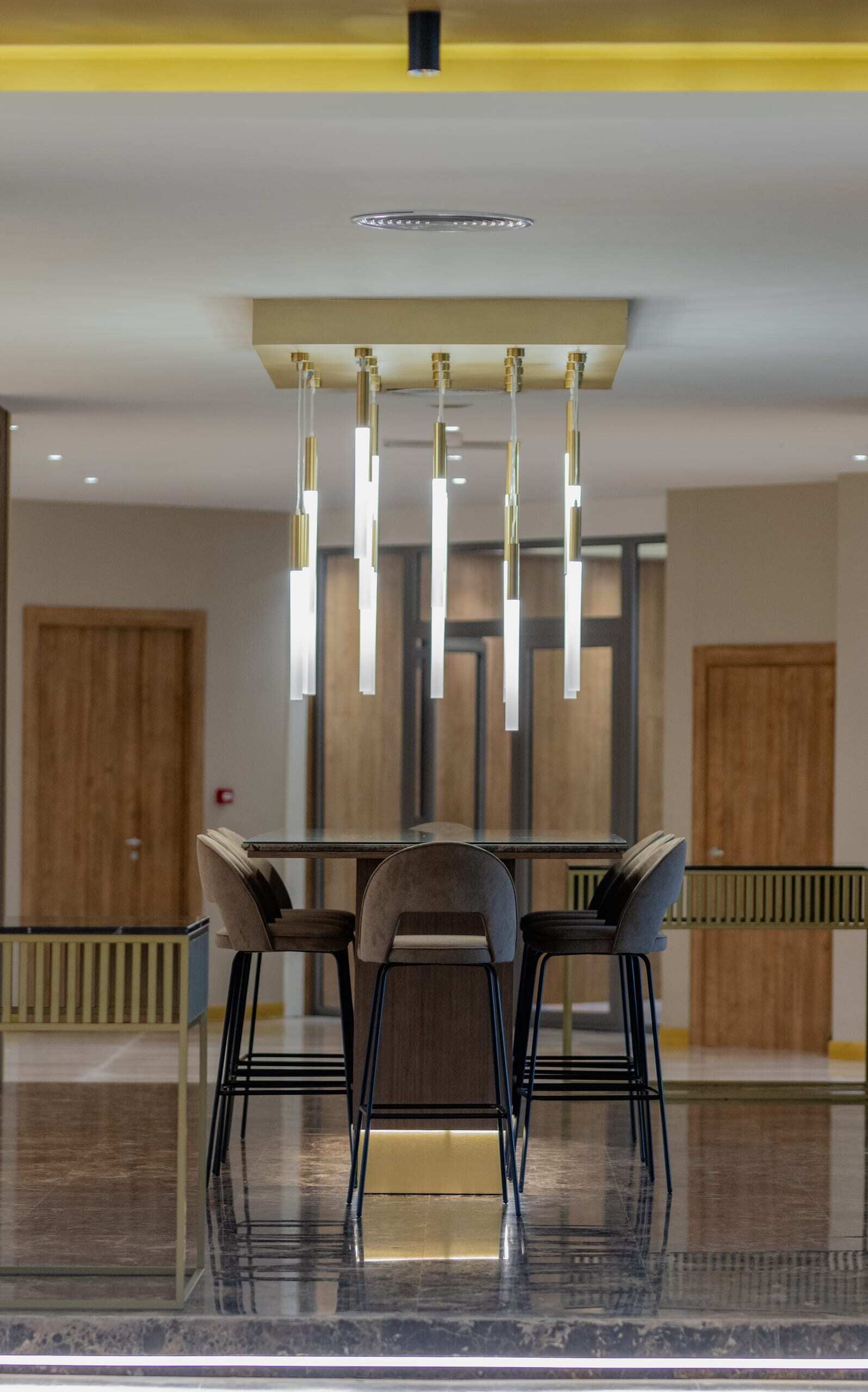 A modern dining area with a rectangular table and four chairs, a hanging light fixture, and wooden doors in the background.
