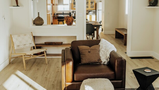 Ein modernes Wohnzimmer mit einem braunen Ledersofa, einem Holzstuhl und einem schwarzen Beistelltisch.