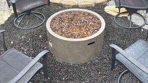 Ein Feuerkorb, umgeben von vier Metallstühlen, mit Kiesfläche.