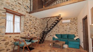 Una habitación con paredes de piedra, una escalera, un sofá color turquesa, una mesa de comedor de madera y sillas.