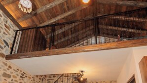 Un interior rústico con pared de piedra, escalera de madera, sofá color turquesa y mesa de madera.