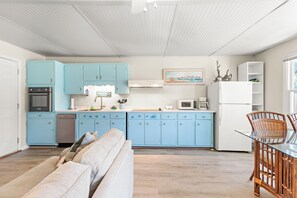 Une cuisine moderne avec des meubles de couleur bleu clair, un réfrigérateur blanc et un coin repas doté de chaises en osier.