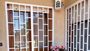 A patio with two chairs, a round table, and a window with white shutters. - Tatina's Sunny Apartment. Your home near the sea. (Palermo)