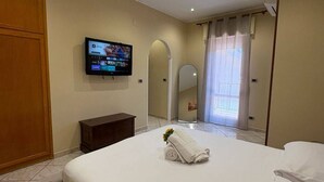 A hotel room with a bed, a TV mounted on the wall, a mirror, and a window with curtains. - Tatina's Sunny Apartment. Your home near the sea. (Palermo)