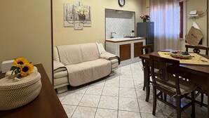 A living room with a sofa, a dining table with chairs, a kitchen area with a refrigerator, and a clock on the wall. - Tatina's Sunny Apartment. Your home near the sea. (Palermo)