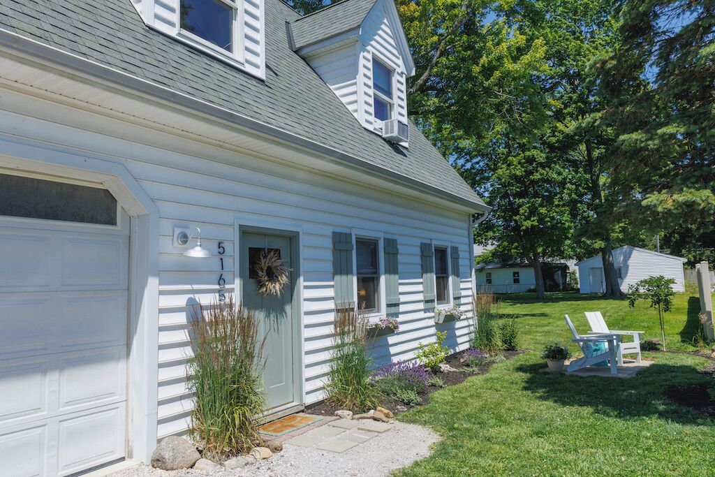 A white house with a garage, a front door, and a small garden with a lawn chair.