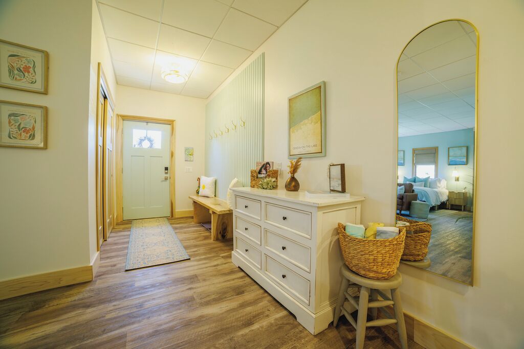 A hallway with a wooden floor, a white dresser with drawers, a mirror, and a bench.