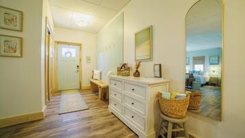 A hallway with a wooden floor, a white dresser with drawers, a mirror, and a bench.